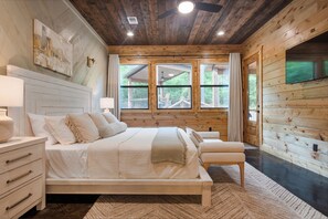 Un dormitorio de cabaña de madera con una cama, mesitas de noche y un televisor.