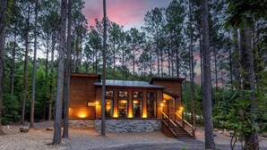 A cabin with a stone foundation, wooden exterior, and a staircase leading to a covered porch. - 21-Ft Swim Spa Pool | 2 King Suites | Game Loft | Playset | Swings | Hot tub (Broken Bow)