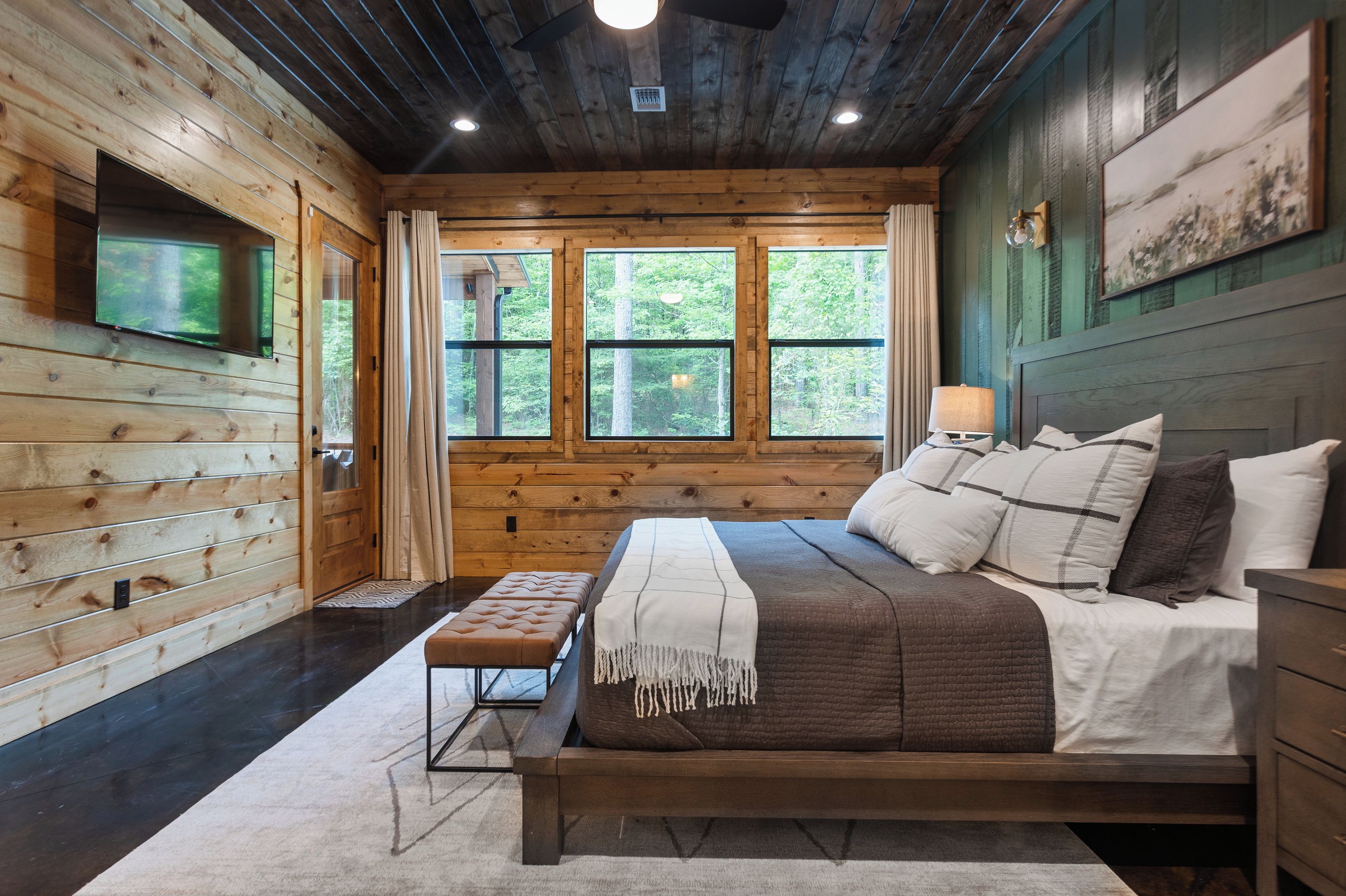 Un dormitorio tipo cabaña de madera con una cama, un banco y un televisor montado en la pared.