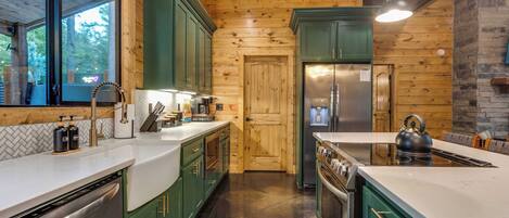 A modern kitchen with green cabinets, stainless steel appliances, and a wooden ceiling.