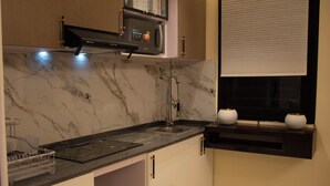 A kitchen with a marble countertop, a built-in oven, a sink, and a window with blinds. - LE DANORE VIP APPART hotel (Yaoundé)