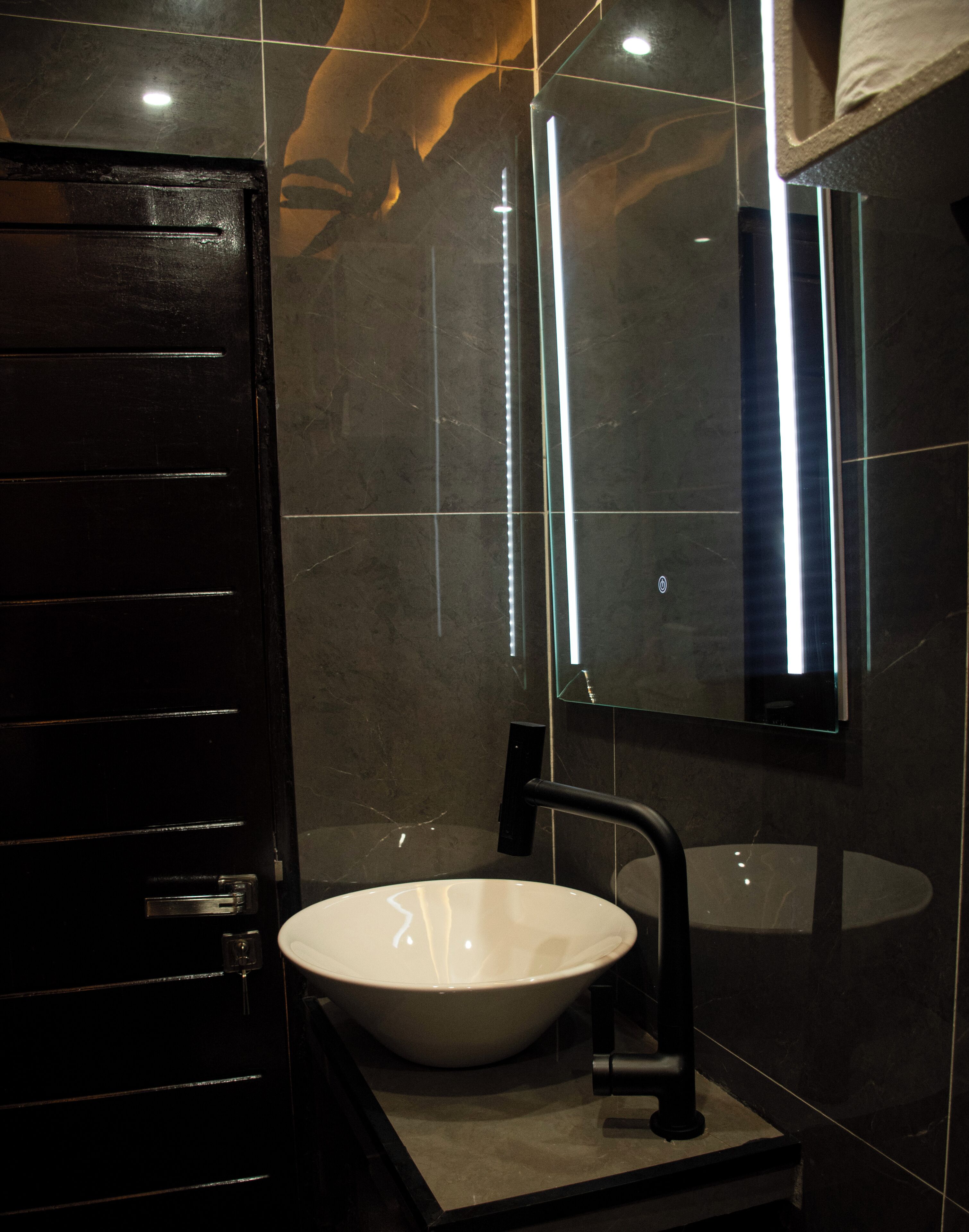 Un baño moderno con una puerta negra, un lavamanos blanco y un espejo.