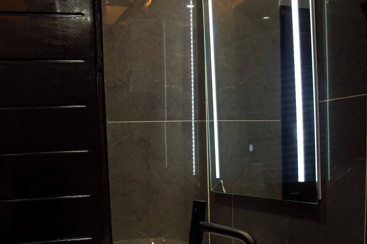 Un baño moderno con una puerta negra, un lavamanos blanco y un espejo.