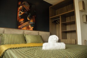 Una habitación de hotel con una cama, un cuadro grande en la pared, un armario de madera y una cama bien hecha con una toalla blanca enrollada.