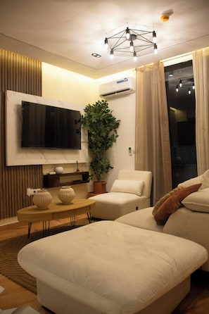 A modern living room with a flat-screen TV, a potted plant, a sofa, and a coffee table. - LE DANORE VIP APPART hotel (Yaoundé)