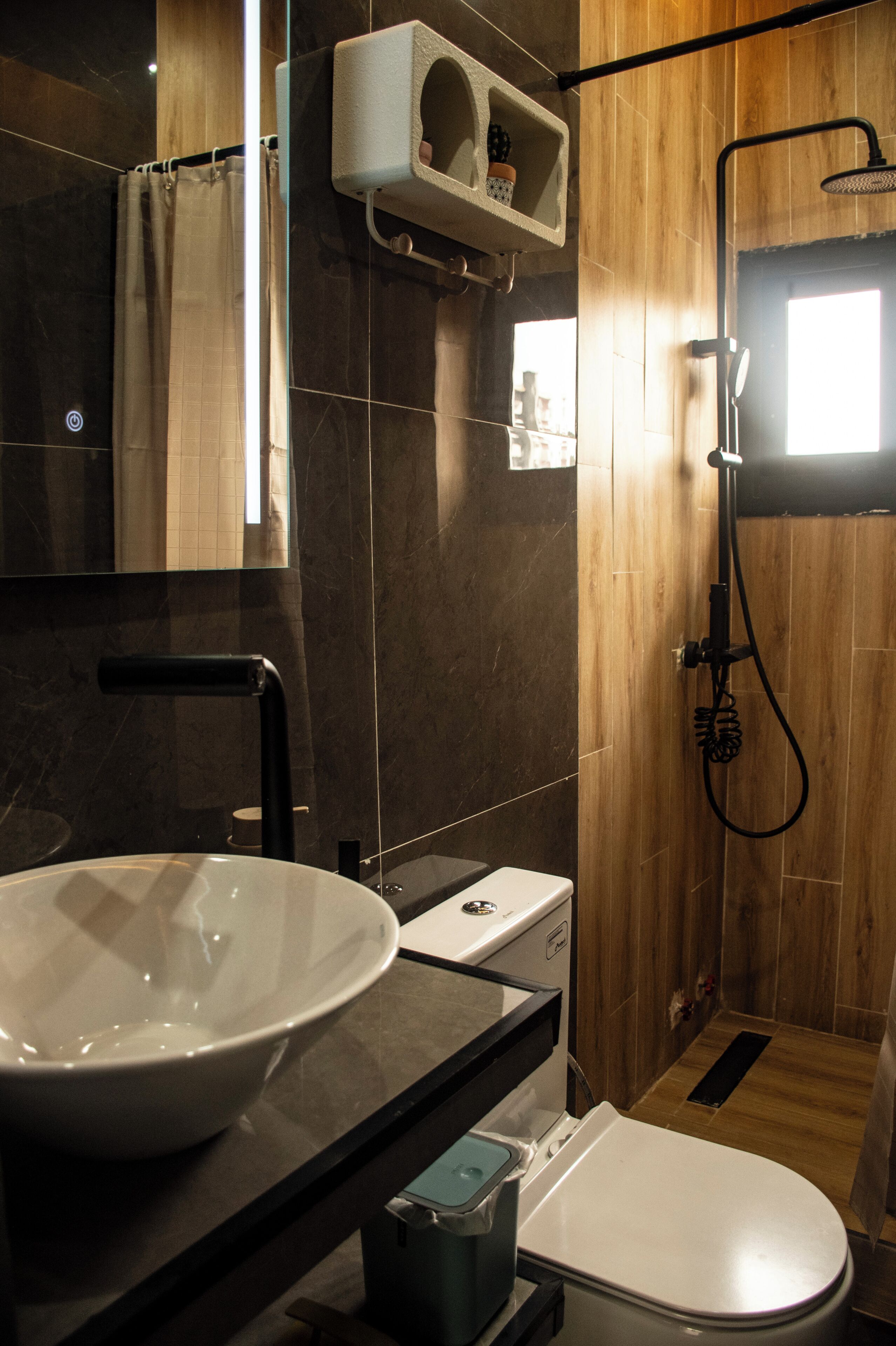 A modern bathroom with a large white sink, a toilet, a shower with a handheld showerhead, and a wooden vanity.