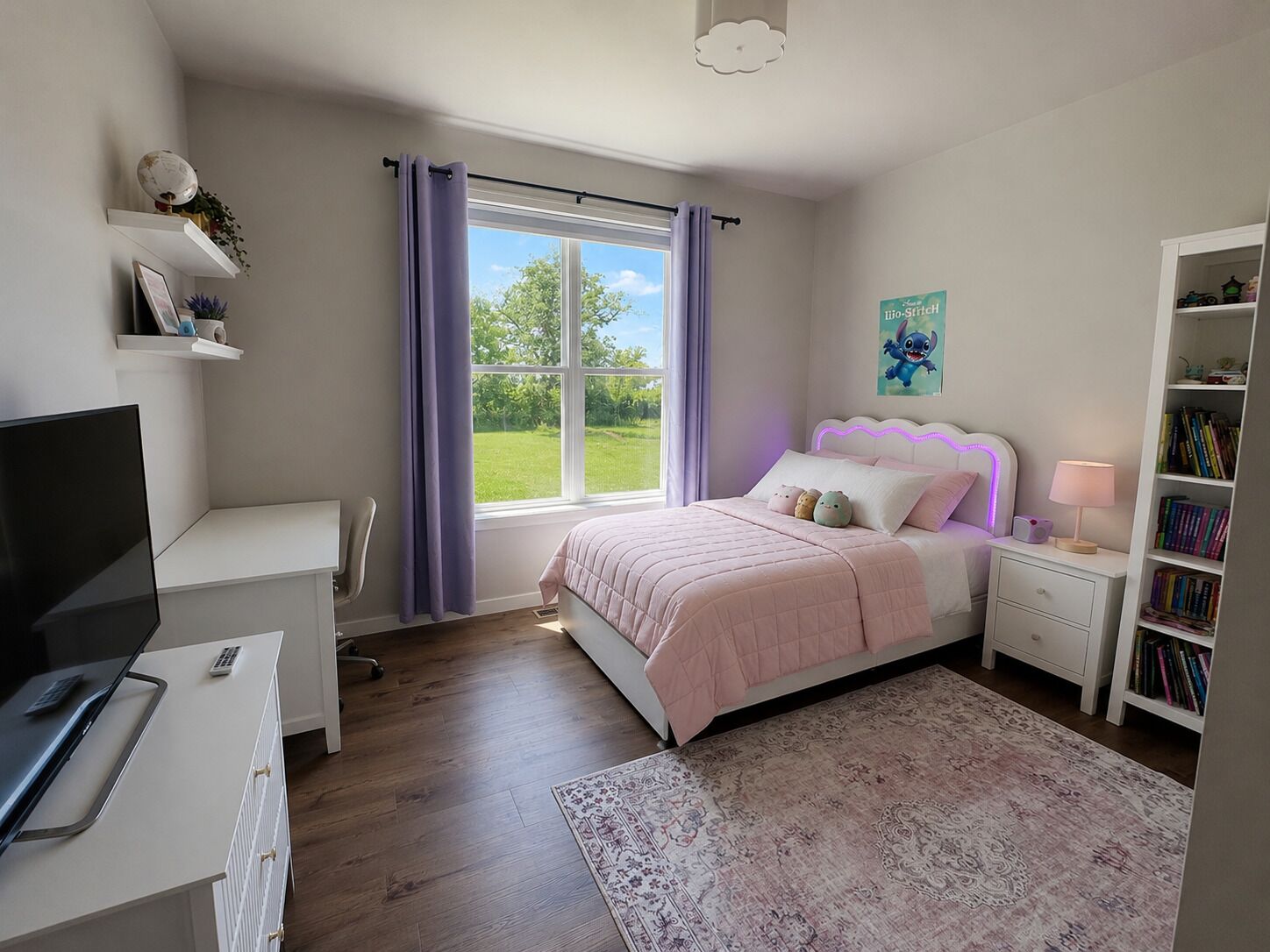Un dormitorio con cama, mesita de noche, lámpara, estantería y un escritorio con computadora.