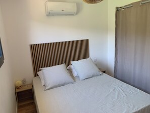 A bedroom with a striped bedspread, a wooden slat headboard, a bedside table with a lamp, and an air conditioning unit. - 65-square-meter house, fully air-conditioned, with a spa (Bormes-les-Mimosas)