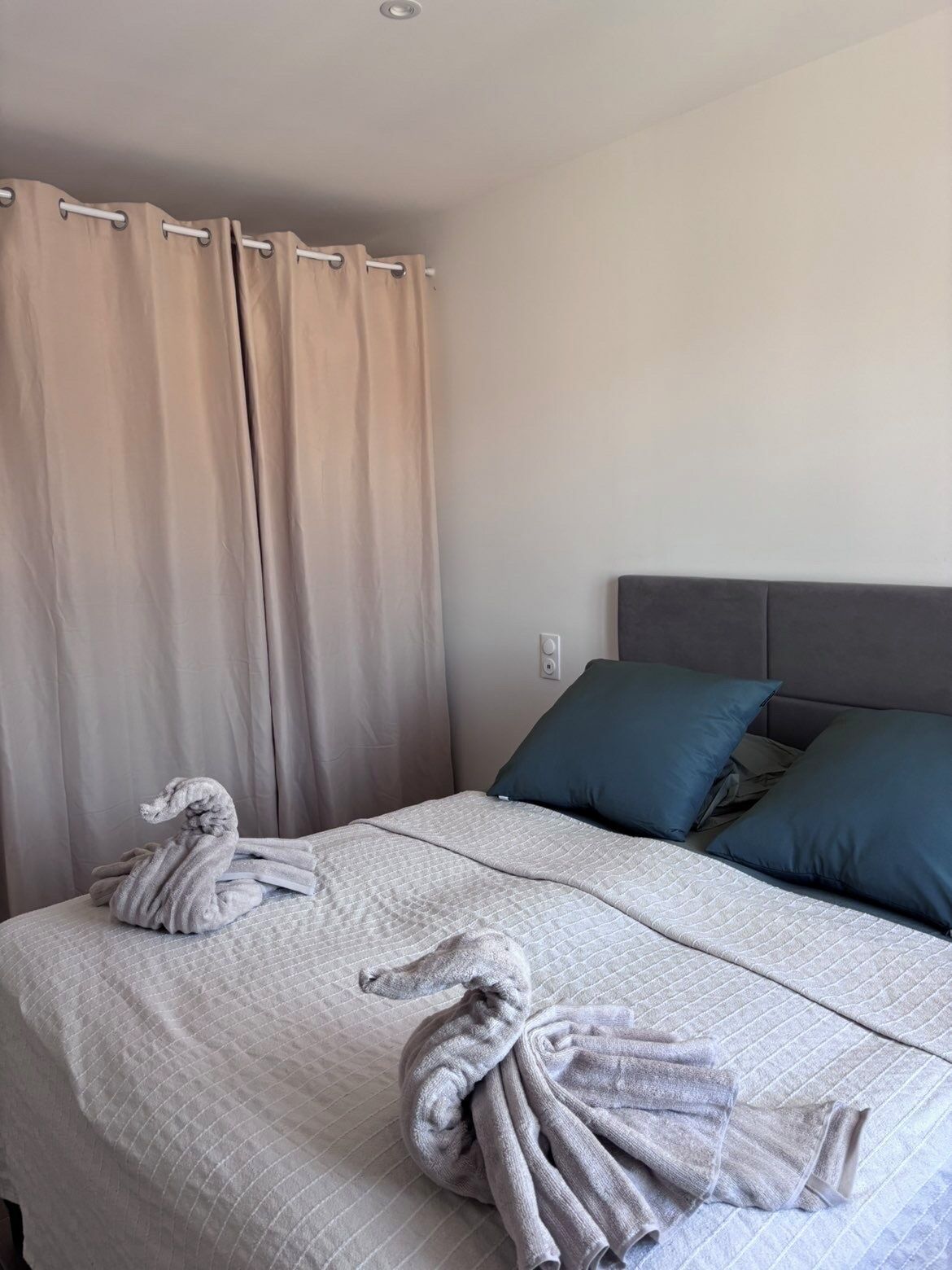 A hotel room with a bed, two pillows, a curtain, and two towels.