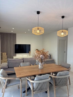 A modern living room with a wooden dining table, grey upholstered chairs, a flat-screen TV, and two hanging wicker pendant lights. - Family villa, not overlooked, with a private pool, a five-minute walk from downtown (L'Isle-sur-la-Sorgue)