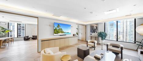 A modern living room with a flat-screen TV, comfortable seating, a dining area, and large windows with a city view.