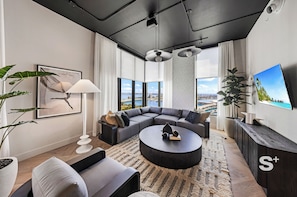 Una sala moderna con un sofá modular, una mesa de centro redonda, un televisor grande y vistas a la ciudad.