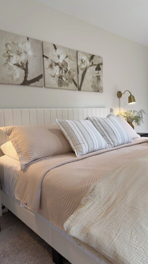 A bed with a beige quilt, pillows, and a headboard. There are three wall-mounted floral paintings above the bed. - 4BR Lexington Home – Pool, Fishing Pond, Firepit, Sleeps 8 (Lexington)