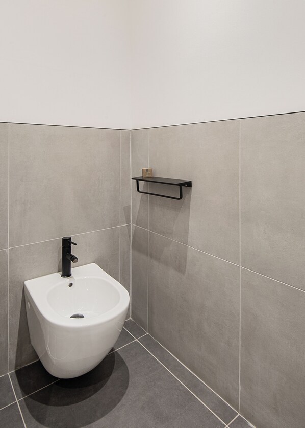 Een moderne badkamer met een wit wandcloset, een zwarte kraan en een klein plankje erboven.