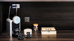 Un mapa de la ciudad enmarcado en una pared, una cafetera, una taza, un hervidor y un caja de madera sobre un estante de madera oscura.