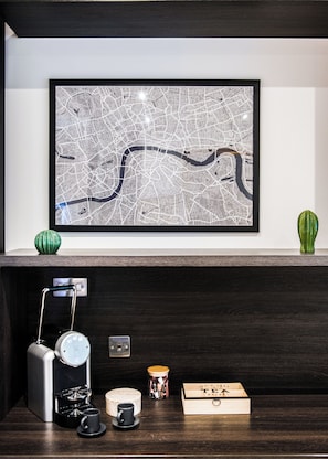A framed city map on a wall, a coffee machine, a mug, a teapot, and a wooden box on a dark wooden shelf. - SomersetHouseSuites by Aureva Residences (London)