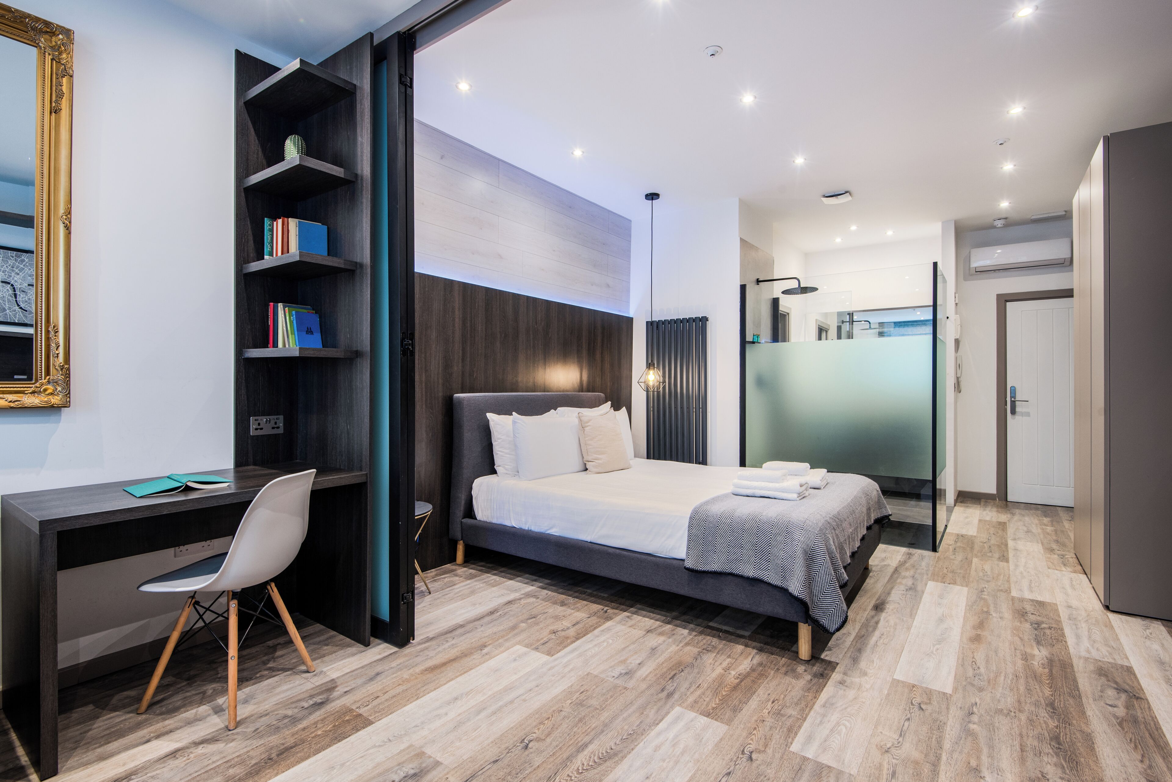 A modern bedroom with a bed, desk, chair, and a bookshelf.