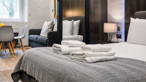 Habitación de hotel con cama, sofá, escritorio y silla. Hay una lámpara en el escritorio y una ventana con vistas a árboles.