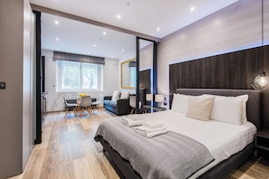 A modern hotel room with a large bed, a dining area, a sitting area, and a large mirror. - SomersetHouseSuites by Aureva Residences (London)