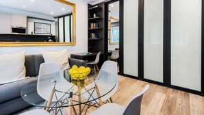 Una sala de estar moderna con una mesa de vidrio, sillas blancas, un sofá y un espejo grande.