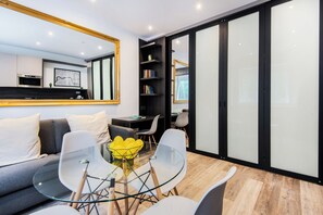 A modern living room with a glass table, white chairs, a sofa, and a large mirror. - SomersetHouseSuites by Aureva Residences (London)