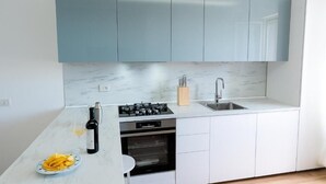 A modern kitchen with white cabinets, a marble countertop, a gas stove, an oven, and a sink. - Apartment Facing the Sea Parking Beach (Porto San Giorgio)