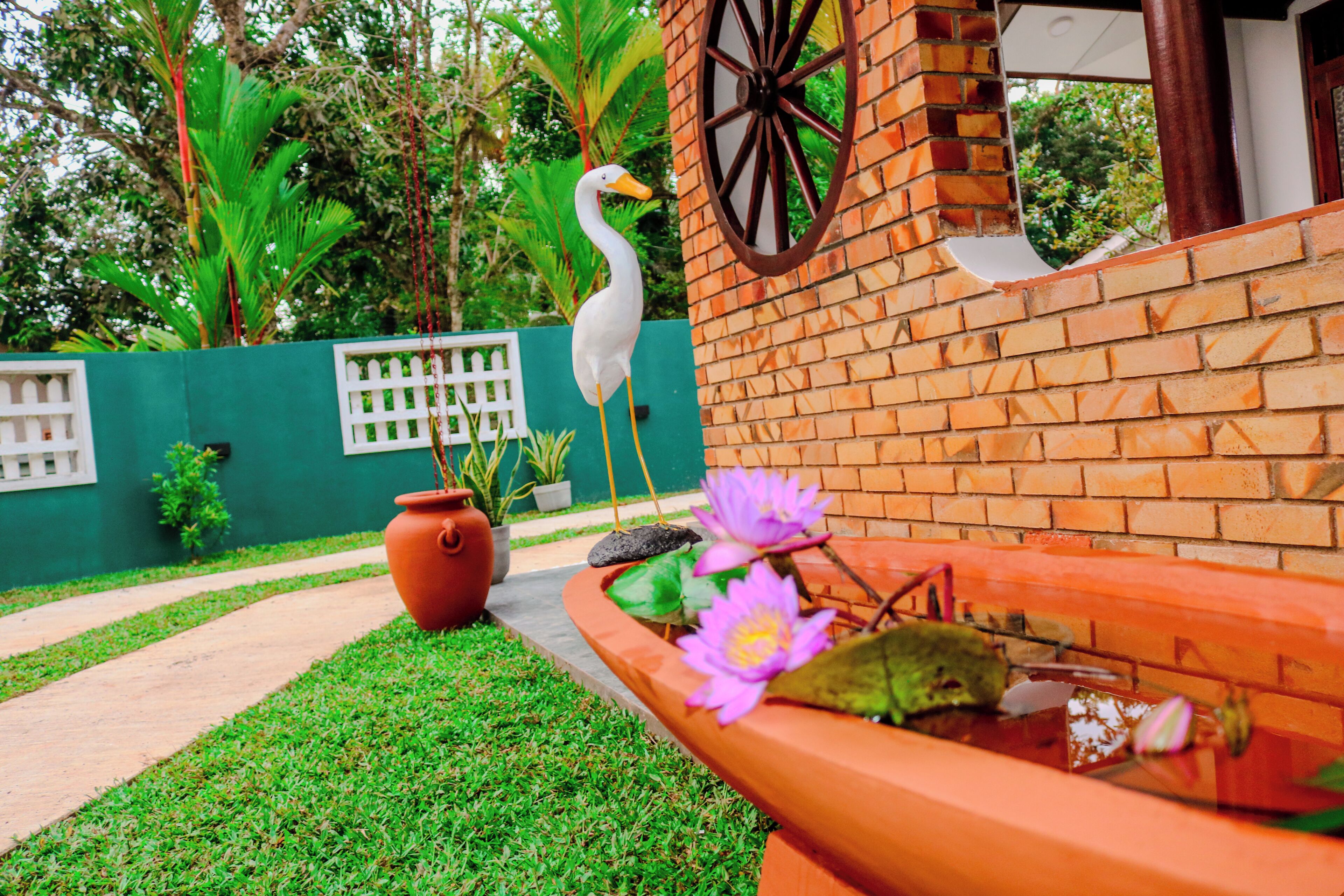 A garden with a white bird, a brick wall, a white fence, and a flower bed with pink flowers.