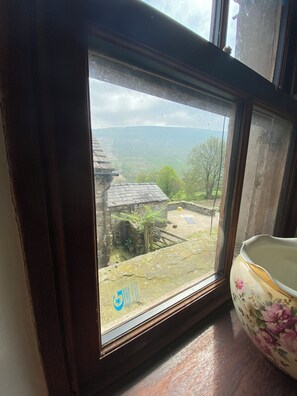 Una ventana con vistas a un paisaje rural, que incluye un edificio de piedra y un árbol.