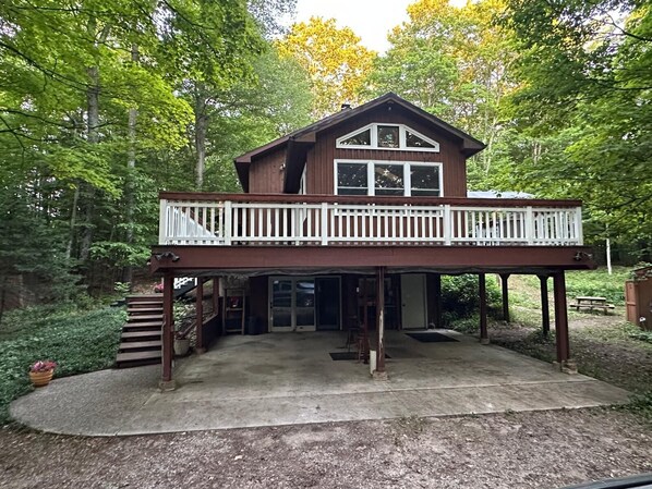 A two-story wooden cabin with a balcony, surrounded by trees.