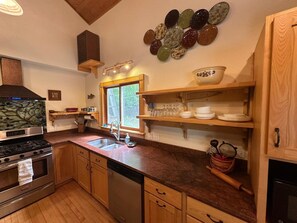 A kitchen with wooden cabinets, a stainless steel stove, a dishwasher, and a window with a view of trees. - Spacious, Private Suttons Bay Oasis in the Woods (Suttons Bay)