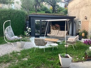 A modern outdoor seating area with a swing chair, a cushioned sofa, and a wooden table. - On the edge of the Jura Lakes, a spacious home with a spa and a pétanque court (Châtillon)