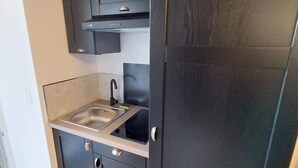 Cocina compacta con muebles oscuros, un lavamanos de acero inoxidable y un grifo moderno.