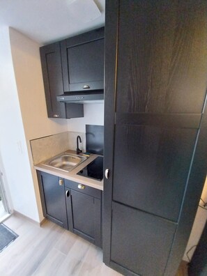 A compact kitchen with dark cabinetry, a stainless steel sink, and a modern faucet. - The "LIBERTÉ" Apartment: A Journey Back to the 1940s (Carentan-les-Marais)