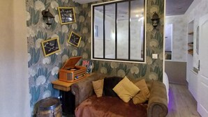 Una sala de estar acogedora con un sofá marrón, un barril de madera, una radio antigua y un ventanal grande.