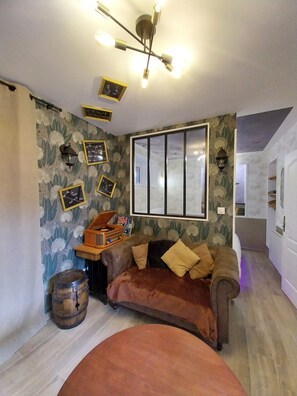 A cozy living room with a brown sofa, a wooden barrel, a vintage radio, and a large window. - The "LIBERTÉ" Apartment: A Journey Back to the 1940s (Carentan-les-Marais)