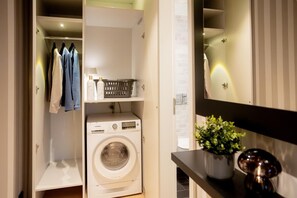 A laundry area with a washing machine, shelves with folded clothes, a basket, and a potted plant. - Liesel's Loft - City Apartment in the heart of the "Water City" of Nordhorn: luxurious and ideal for those seeking relaxation (Nordhorn)