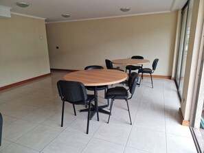 Ein Konferenzraum mit zwei runden Tischen und sechs Stühlen, einem Fliesenboden und einer schlichten Wand mit einer Deckenleuchte.
