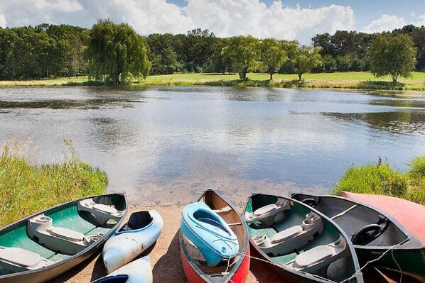 A calm lake with boats docked on the shore, surrounded by trees and greenery.