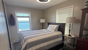 A bedroom with a bed, two bedside tables, a nightstand, a window, a ceiling fan, and a patterned rug.