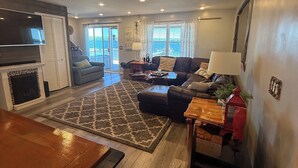 A spacious living area with a fireplace, a sofa set, a dining table, and a view of the ocean through large windows.