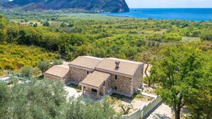 A stone house with a tiled roof, surrounded by lush greenery and a view of the sea and mountains. - Paštrovići Stone Retreat with Pool,Jacuzzi & Adriatic Sea Views (Kaluđerac)