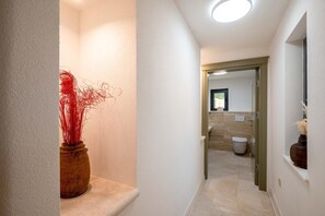 Un pasillo con un jarrón de madera, una puerta que da al baño y un espejo en la pared.