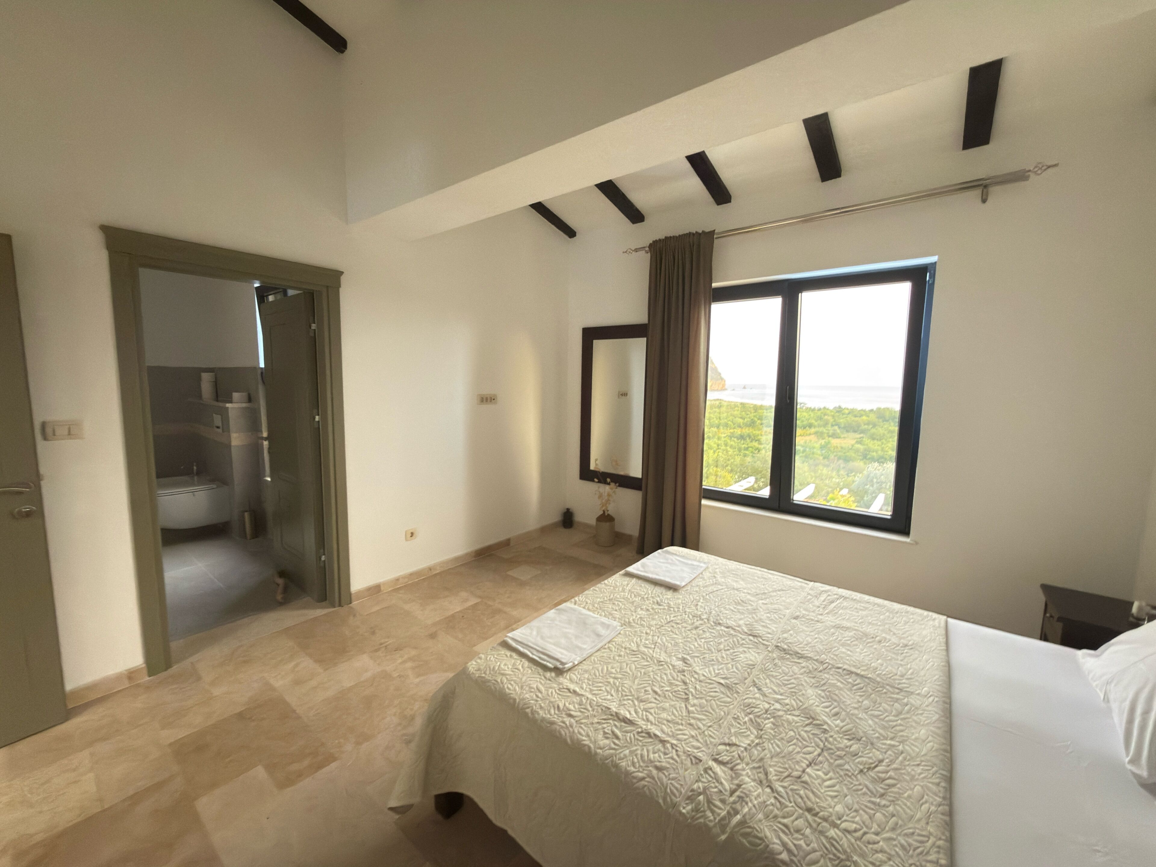 Une chambre à coucher avec un lit, une fenêtre donnant sur un paysage agréable, une salle de bain et une porte menant à une autre pièce.