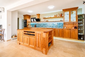 A kitchen with wooden cabinets, a central island with wine storage, a tiled backsplash, and a built-in oven.
