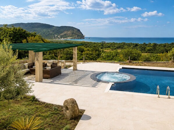 A pool area with a hot tub, outdoor seating, and a view of the sea.