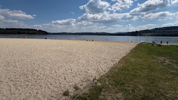 Una platja amb sorra, una zona verda i un llac al fons.