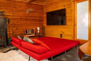 Ein Holzblockhaus-Interieur mit einem roten Sofa, einem Kamin und einem Bücherregal.