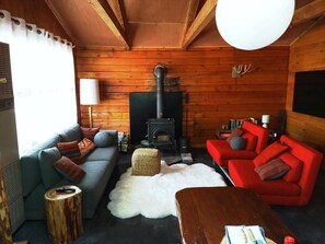 Ein gemütliches Blockhaus-Interieur mit Kamin, Holzwänden, einer Couch, einem roten Sessel und einem Couchtisch.