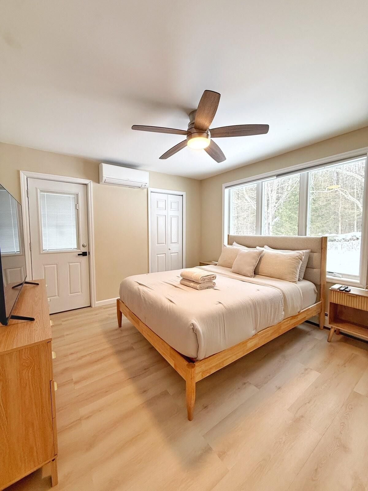 A bedroom with a bed, a ceiling fan, a TV stand, and a window.