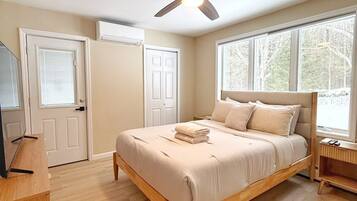 A bedroom with a bed, a ceiling fan, a TV stand, and a window.